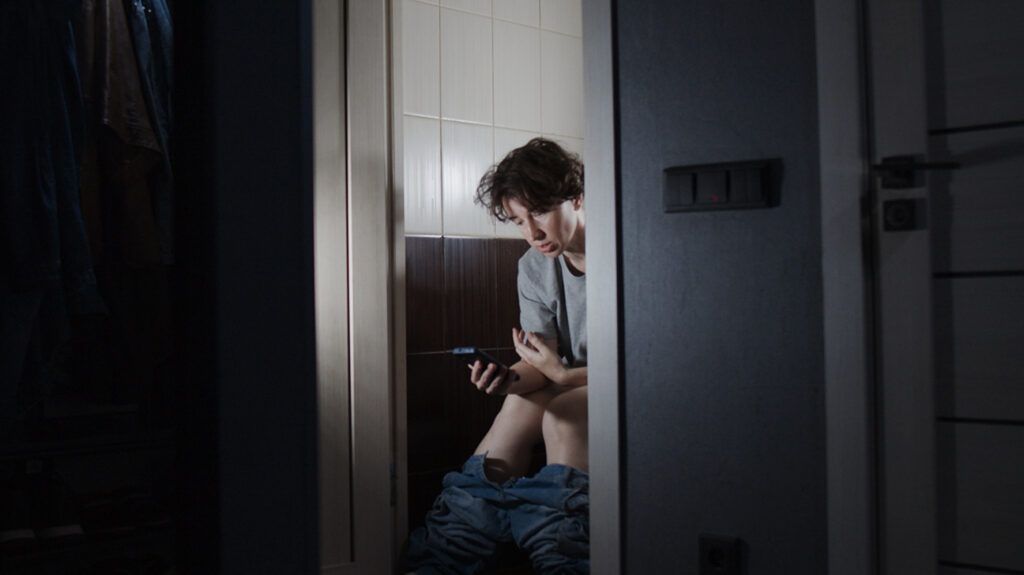 A person with anal skin tags sitting on a toilet and using a smartphone.-2