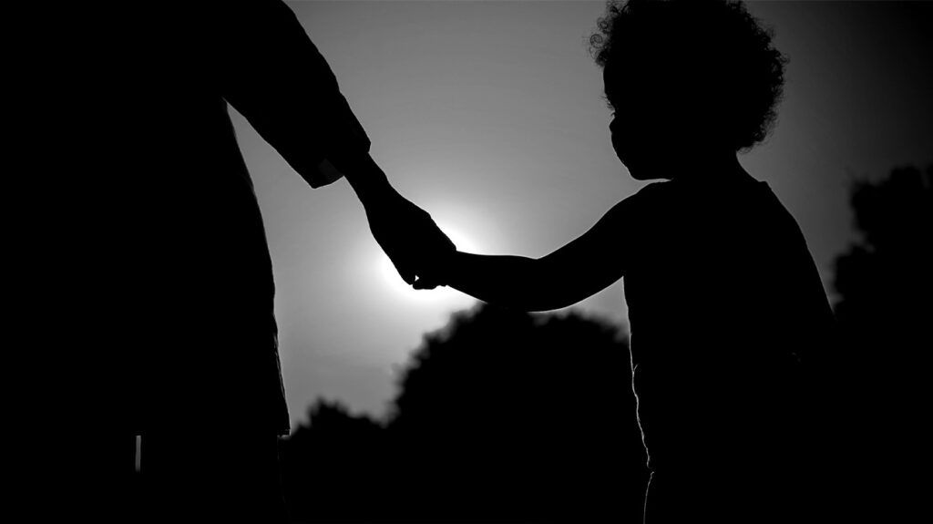 Silhouette of a child holding an adult's hand outside.