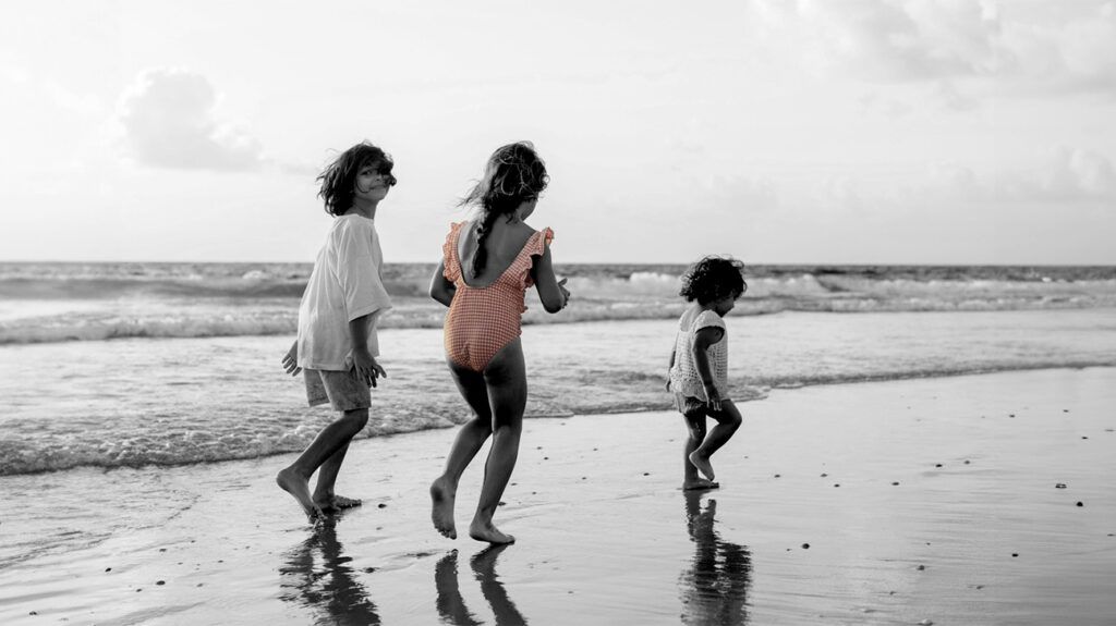 Three siblings of different ages playing on the beach, representing birth order theory. -1