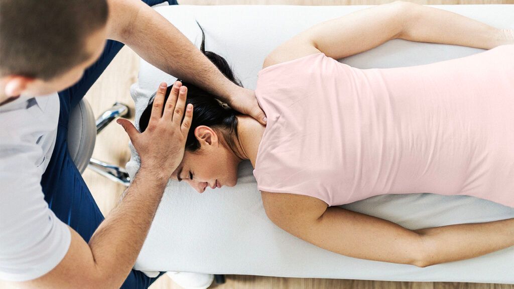 A person lying on their front with a chiropractor performing spinal manipulation on their neck and head.-2