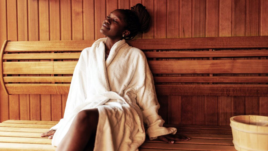 A woman sits in a sauna wrapped up in a bathrobe