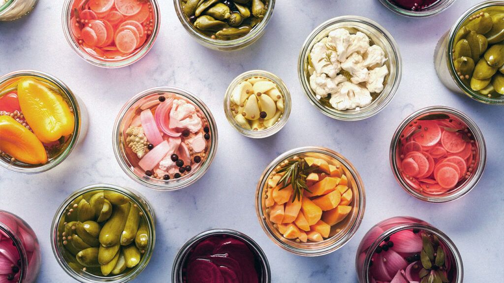 Clear glass bowls full of colorful, fermented, pickled vegetables against a white marble background.