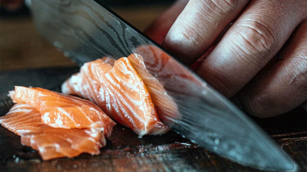 A person slicing raw salmon on a chopping board