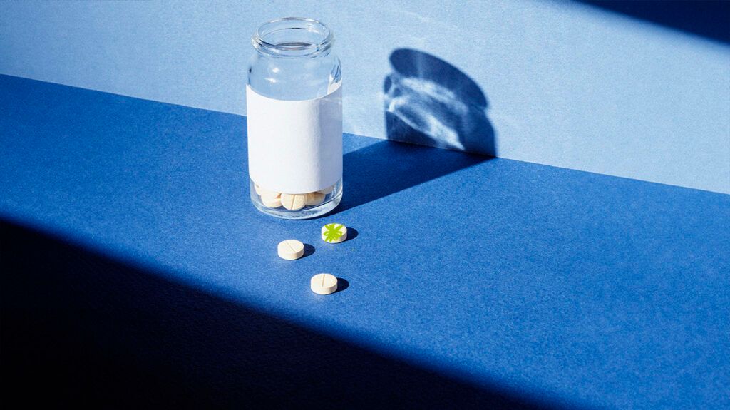 A pill bottle and three pills against a blue background