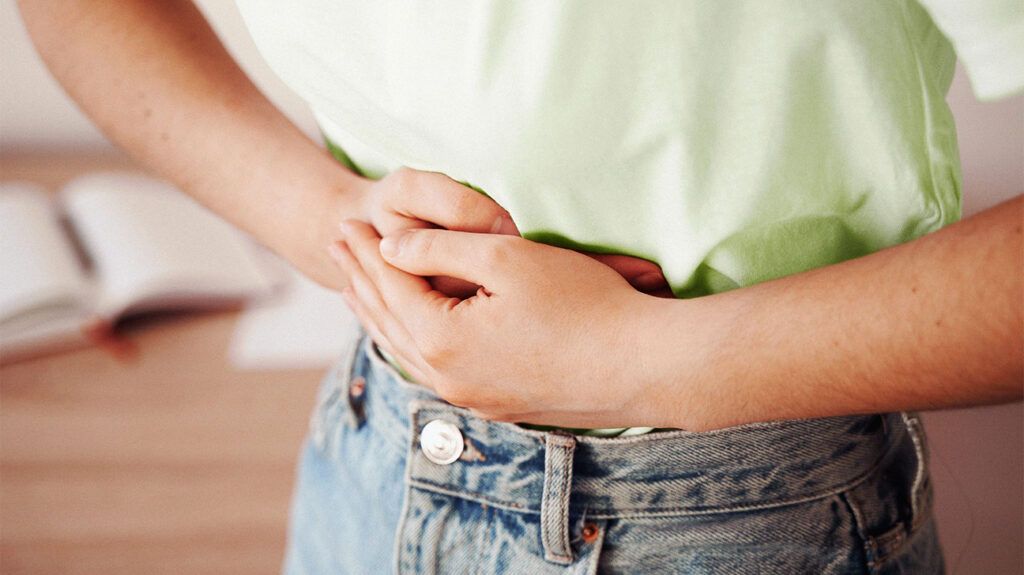 A person with ankylosing spondylitis holding their stomach due to bloating.-2