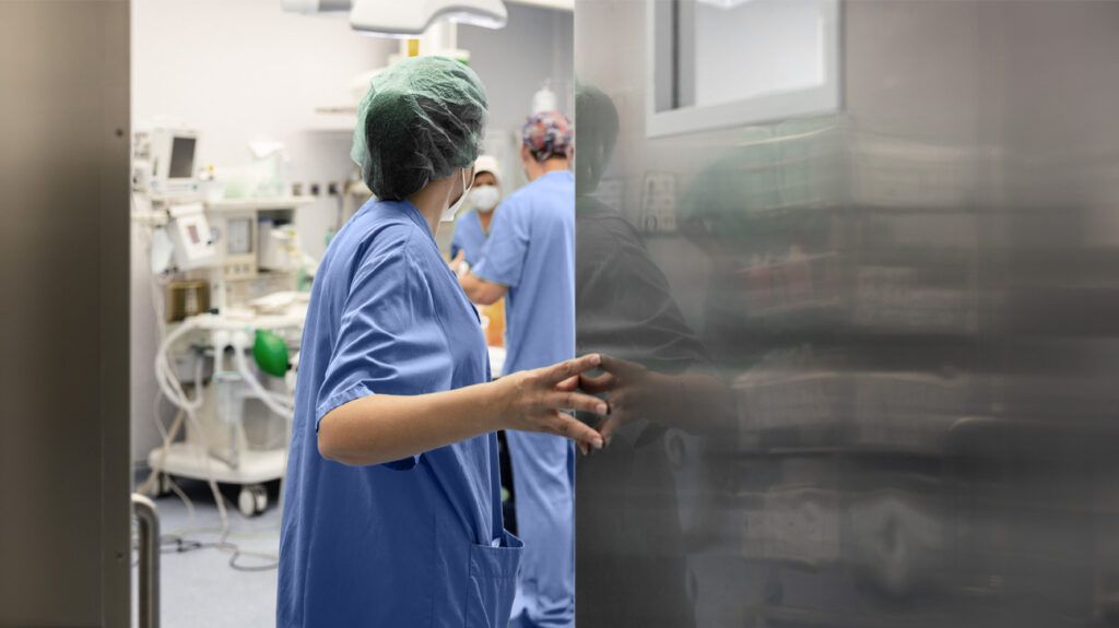 A surgeon entering an operating theatre wearing blue scrubs.