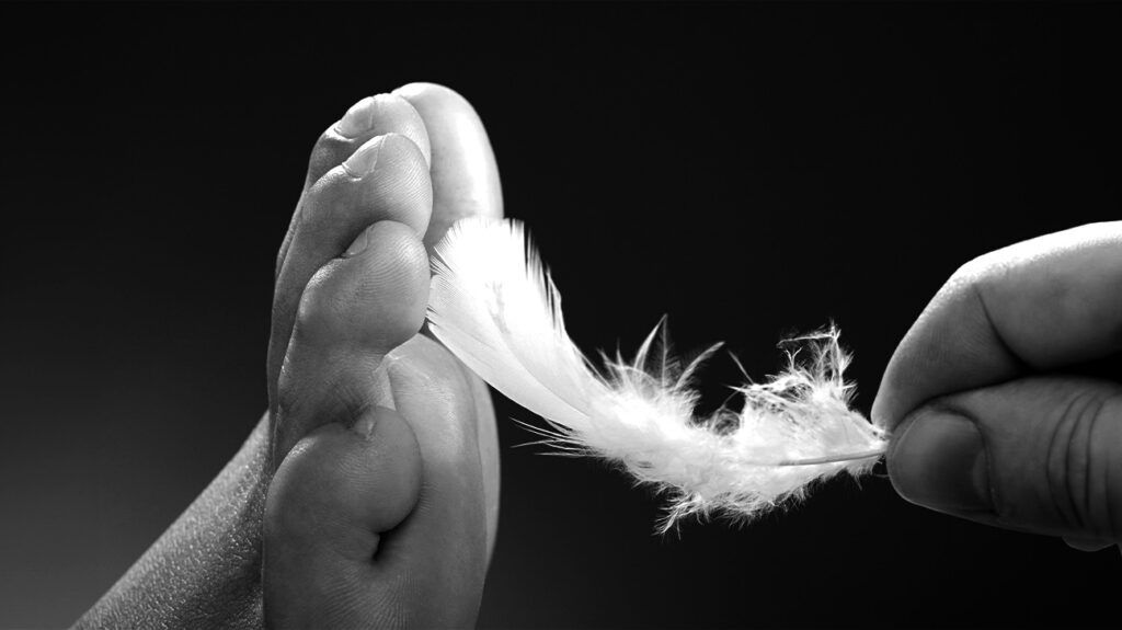 Black and white image of a person's foot being tickled by a feather