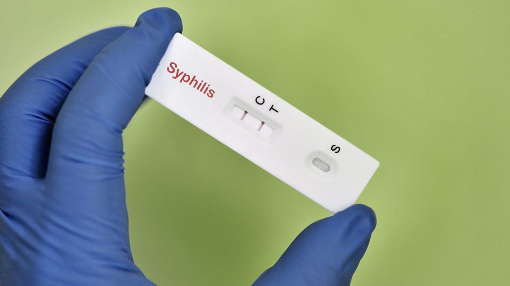 Gloved hand holding a syphilis test against a green background