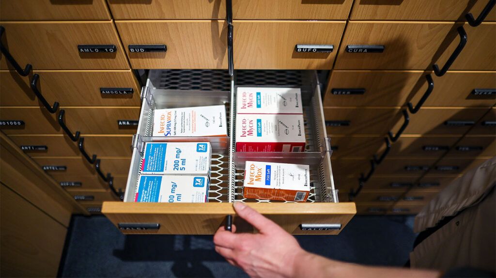 Person's hand opening a drawer of medications in a pharmacy