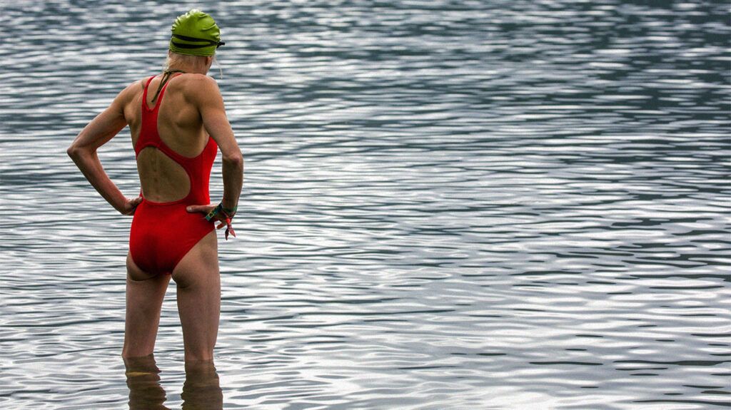 A female swimmer gets ready to swim in a body of water outside, standing in water up to knee height