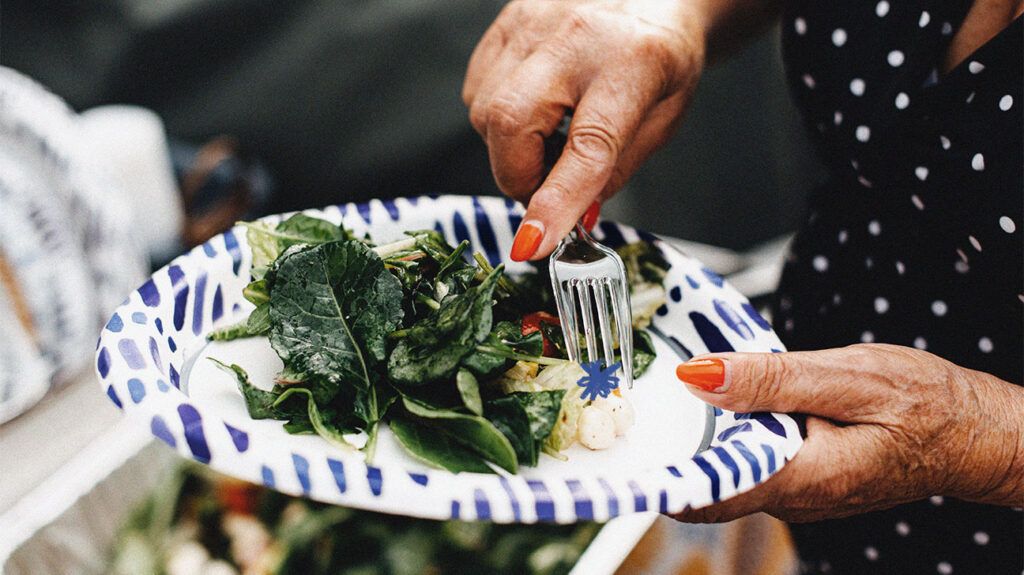 One older adult eating a salad rich in fiber on a paper plate