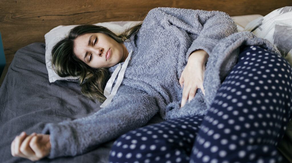 A girl wearing pyjamas lying on her side with PMDD and endometriosis pain. -1