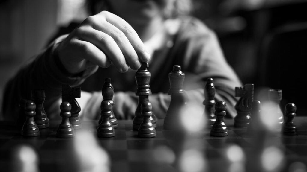 black and white close-up photo of person's hand hovering over chess pieces