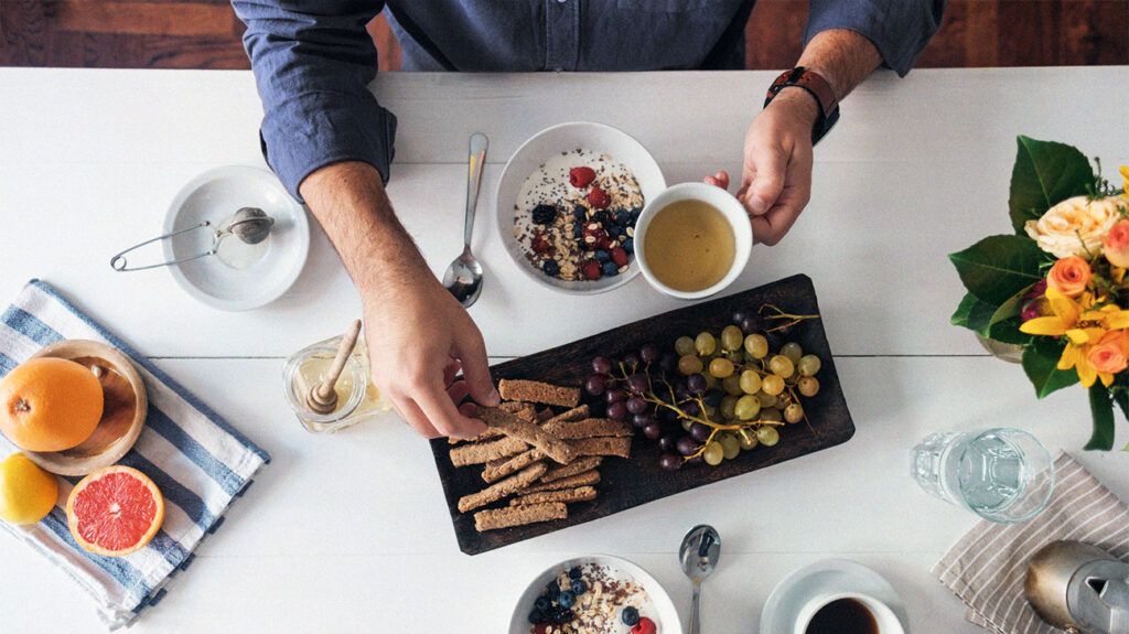 a flatlay of a breakfast table featuring tea, grapefruit, oats and berries, crackers, and different kinds of grapes depicting a meal full of fiber