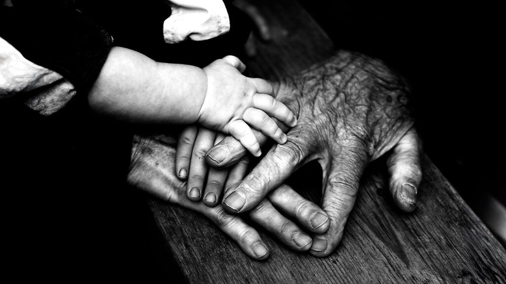 The hands of a grandparent, parent, and child touch