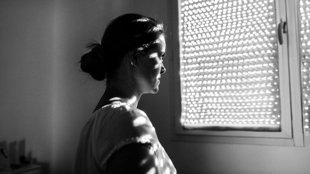 Black and white image of a female looking out a window
