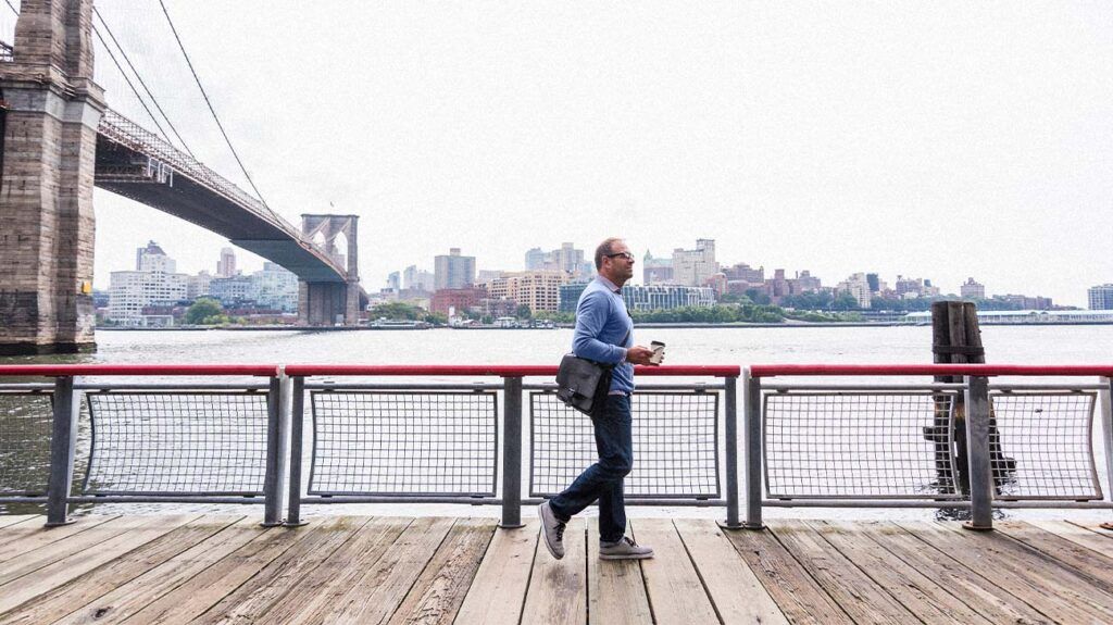 Man walking by the Brooklyn Bridge holding a coffee