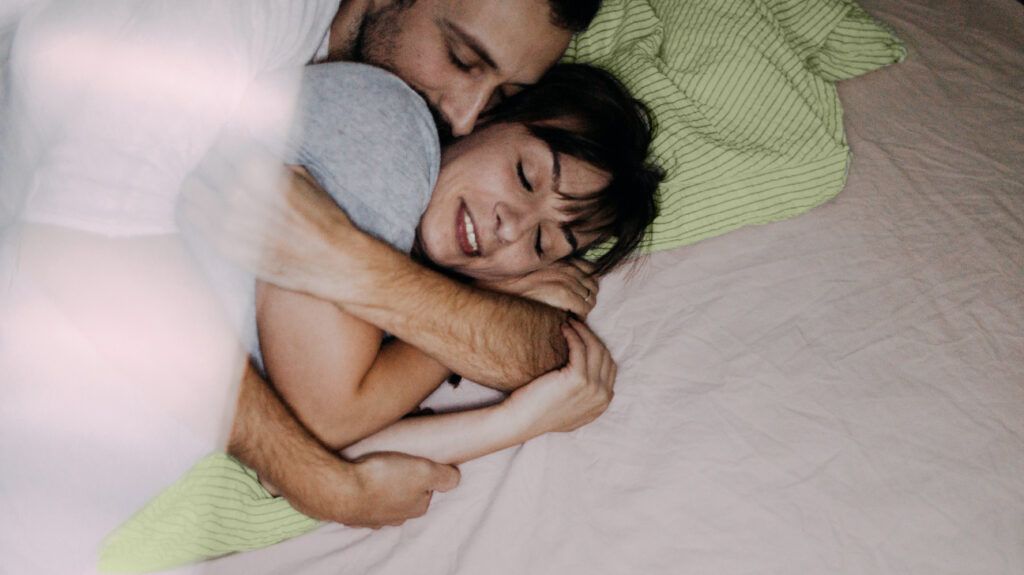 A man and woman cuddling in bed.