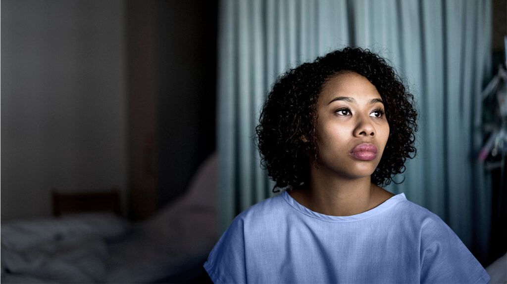 A thoughtful woman sitting in a hospital bed, weighing up the pros and cons of a hysterectomy for endometriosis. -1