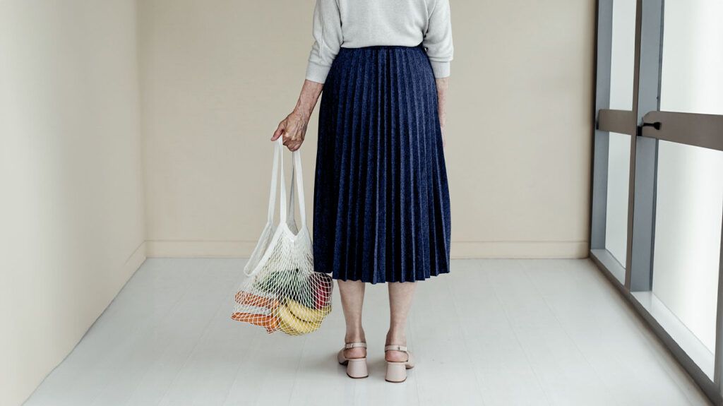 A woman holding a fabric grocery bag full of vegetables and fruits.