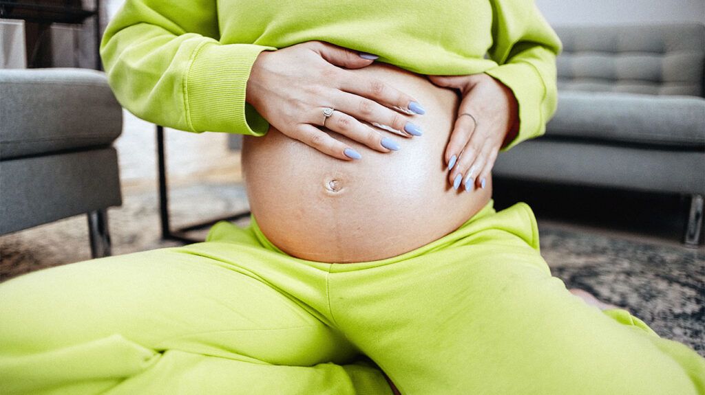 A pregnant woman in a green sweatsuit holds her stomach