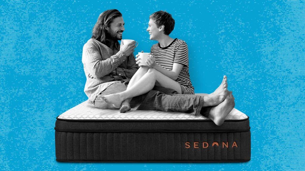 A man and a woman sitting on the Brooklyn Bedding Sedona mattress against a textured blue background.