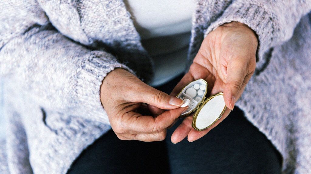 close-up of older person's hands taking pills out of pill box