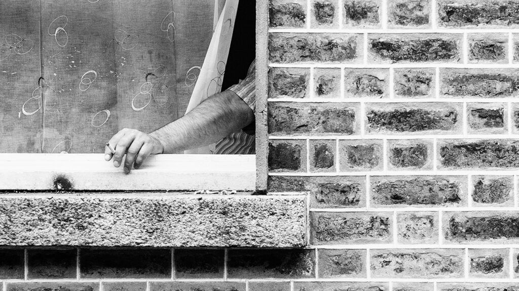 Black and white image of a person holding cigarette out of a window