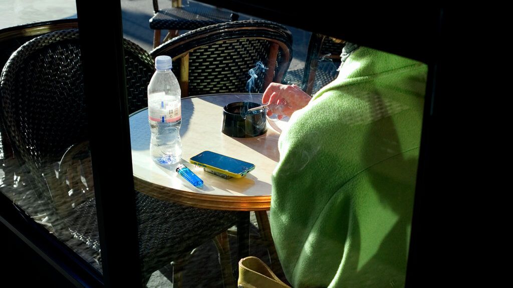 Person sitting at a table outside with a cigarette