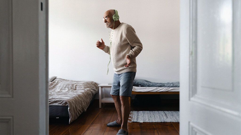 older man wearing spectacles dancing at home with headphones