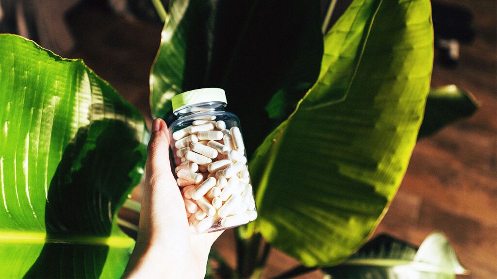 A hand holding a bottle of vitamin d supplements with plants in the background