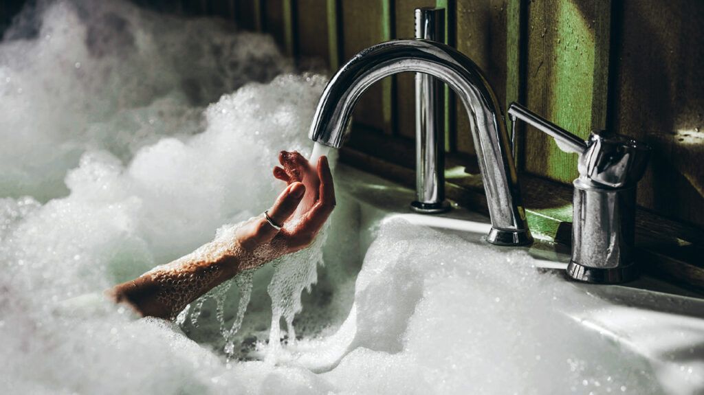 A person with ablutophobia holding their hand under a running tap in a bath.-2