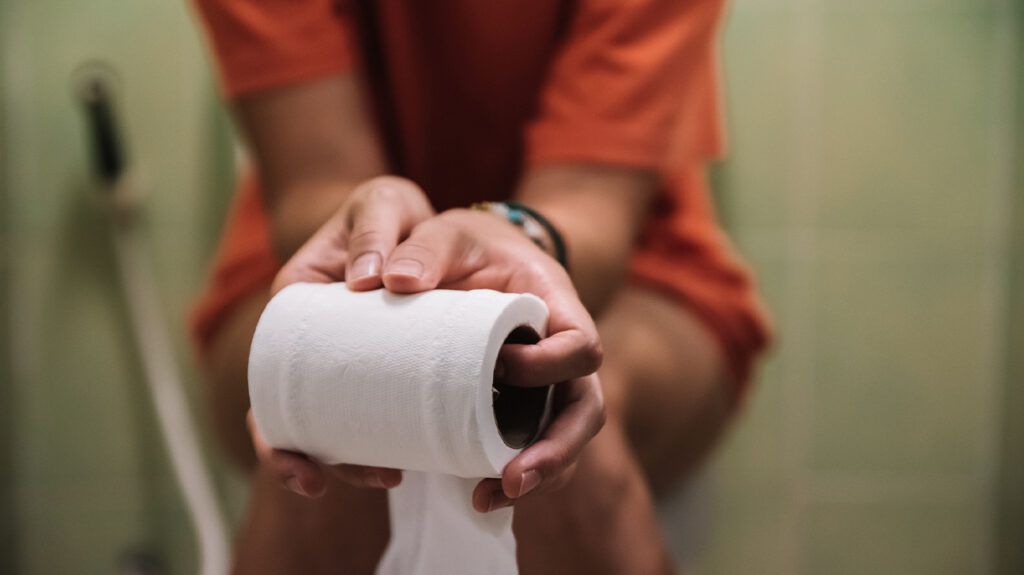 A woman wearing orange, sitting on the toilet and holding a roll of toilet paper -2.