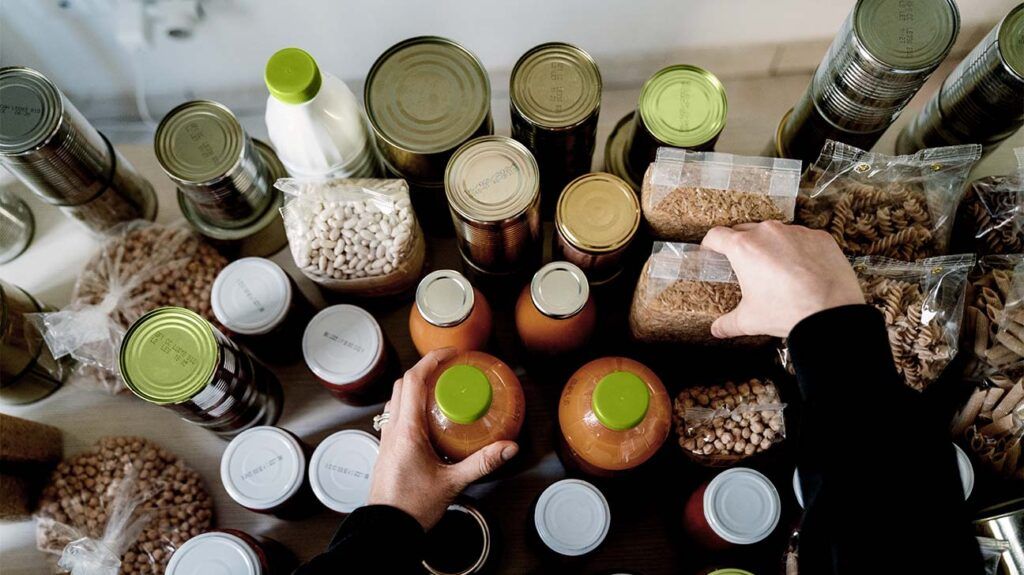 hands arranging packets of beans, canned foods, and bottles of salsa