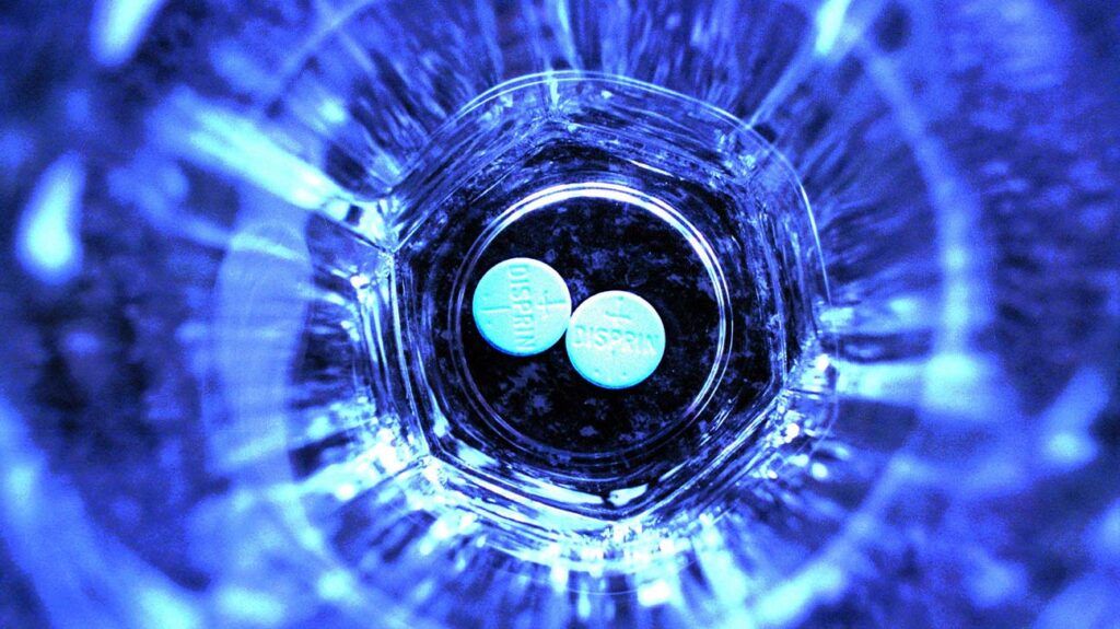 Two aspirin tablets at the bottom of a glass, viewed from above