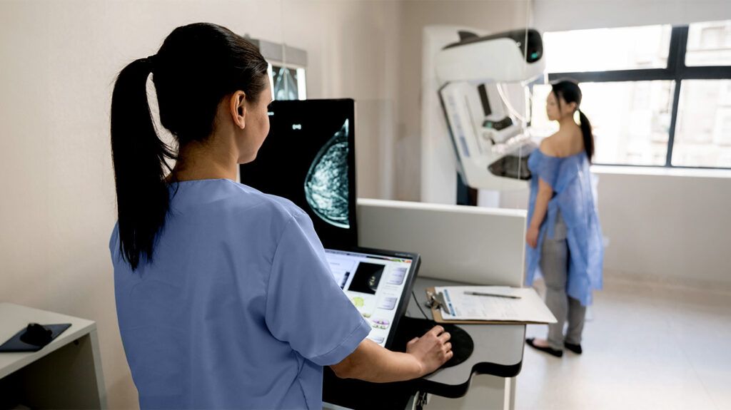 A lab technician looks on as a woman receives a mammogram