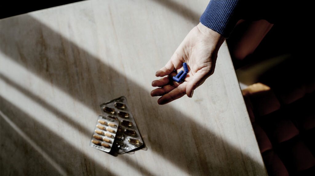 A person holds some blue pills in their hand