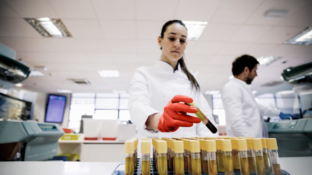 Two scientists in a lab while one places a test tube among vials of blood