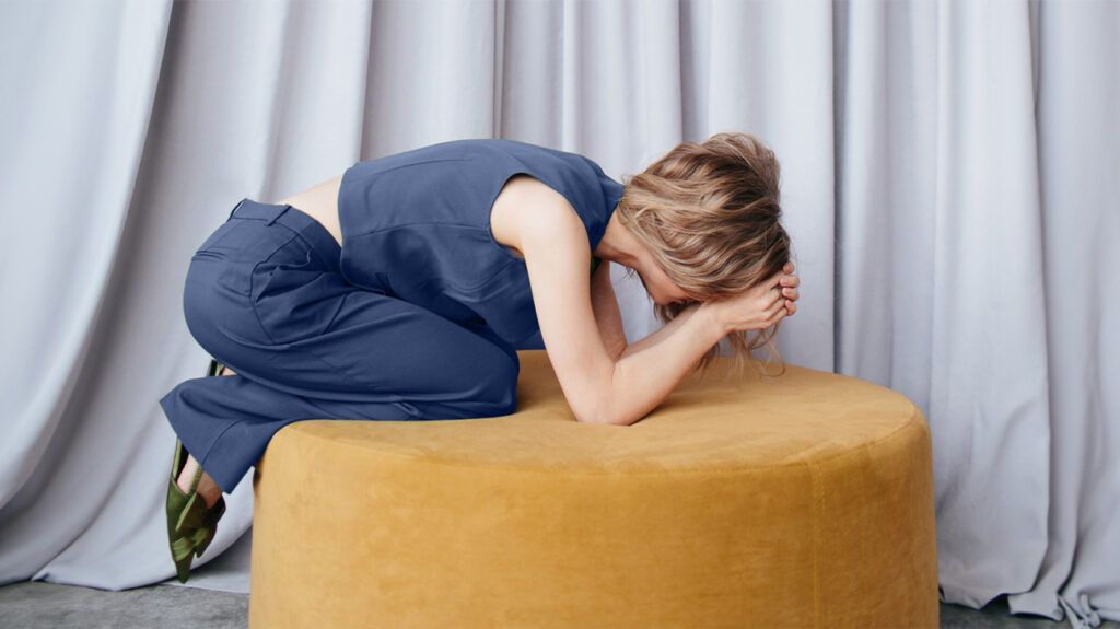 A person with anxiety and gastrointestinal symptoms hunched over on a stool.-1