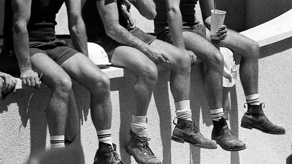 A group of men sitting with their legs dangling off a wall. -3