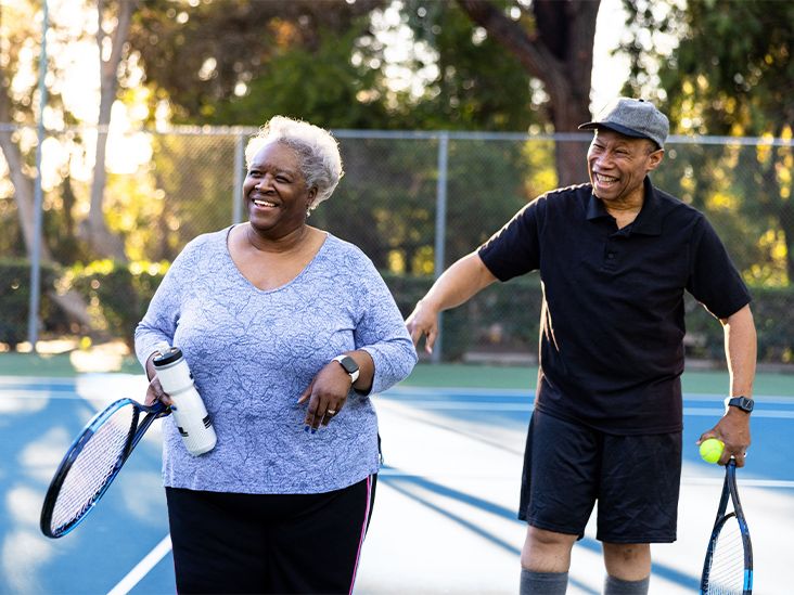 An older adult couple laughing and having fun while playing tennis at the tennis courts.