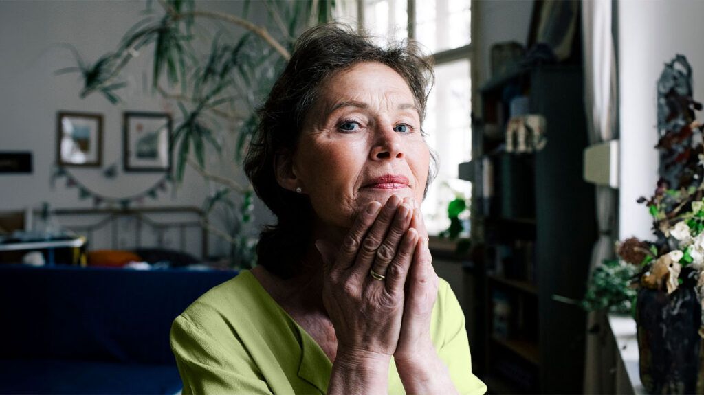 An older adult woman looks pensively as she rests her chin on her hands cupped together