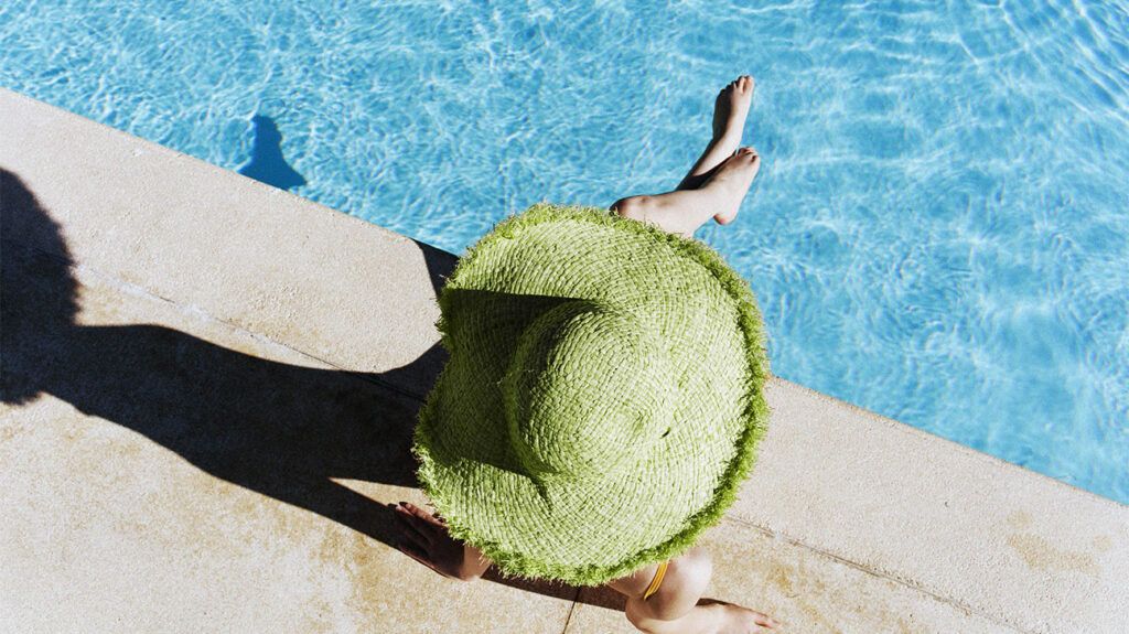 A person who may have used sun protection steps wearing a large sunhat and sitting beside a pool in the sun.-2