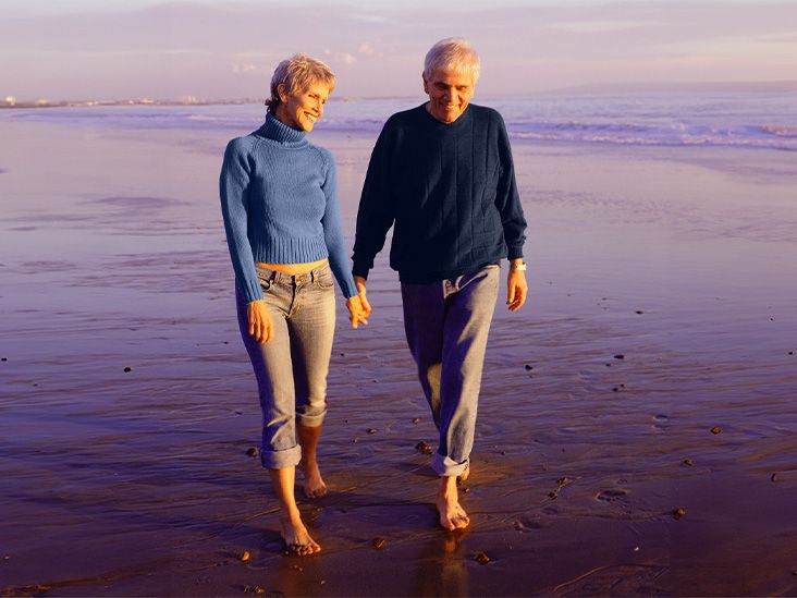A senior couple walking along the beach holding hands.