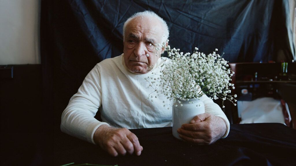 An older adult male touching a flower pot placed in front of him on a flat surface