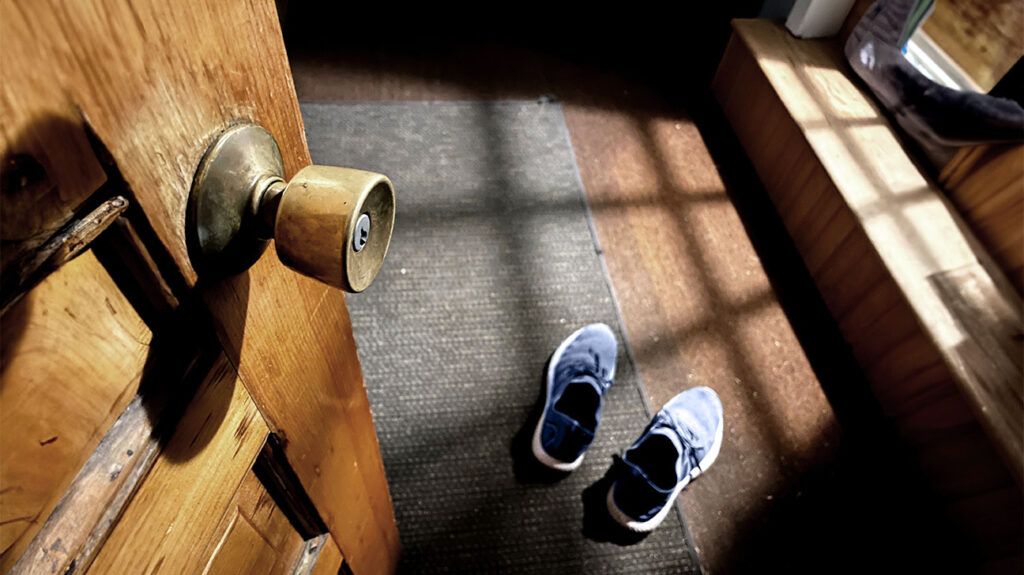A pair of tennis shoes on a floor mat inside an open door