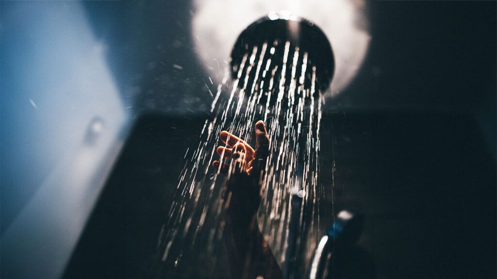 Person's hand under a running shower