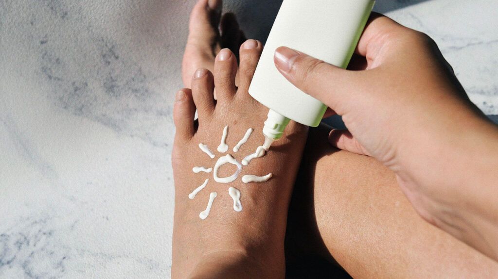 Closeup of a person applying sunscreen on their foot in the shape of the sun.
