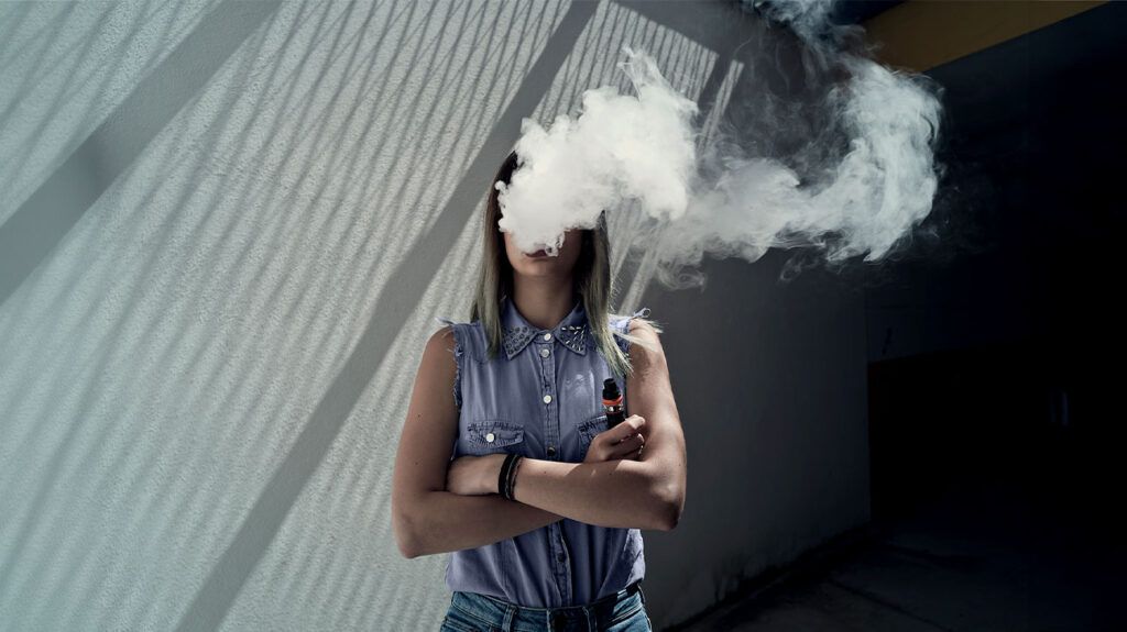 A woman vapes as a cloud of smoke covers her face