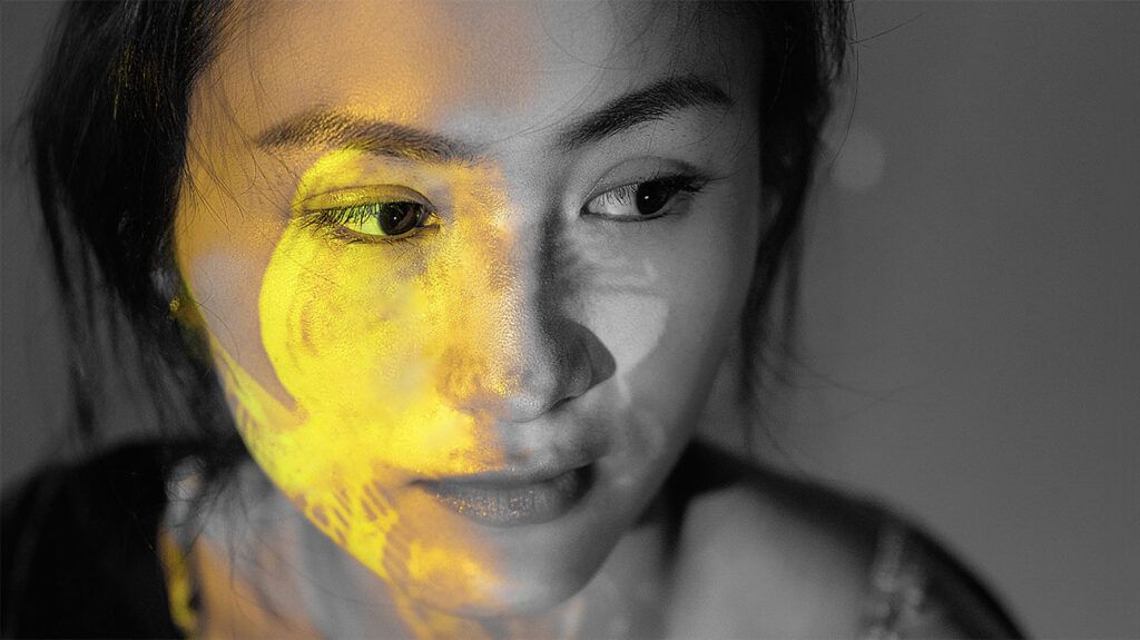 Closeup of a person's face with a yellow light over their cheek and eye.